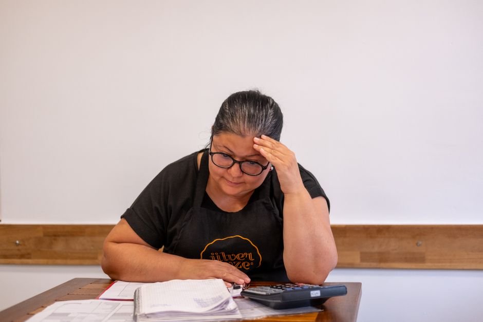 Adult woman looks stressed while working on finances with calculator and notes at a desk.